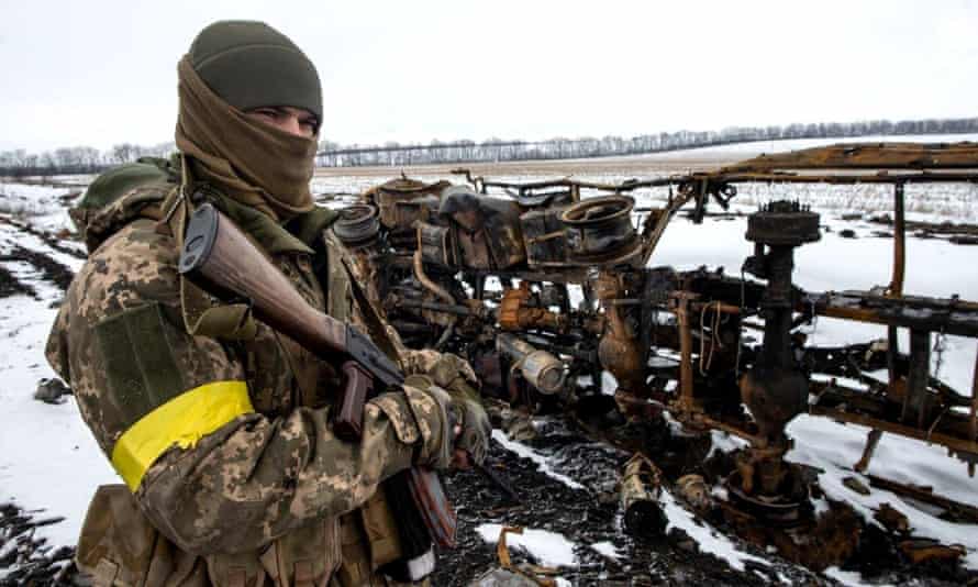 Biden’s impossible bind: how should the US tackle Russia’s invasion of Ukraine? | Joe Biden 1 soldier with gun and yellow armband stands next to supplies