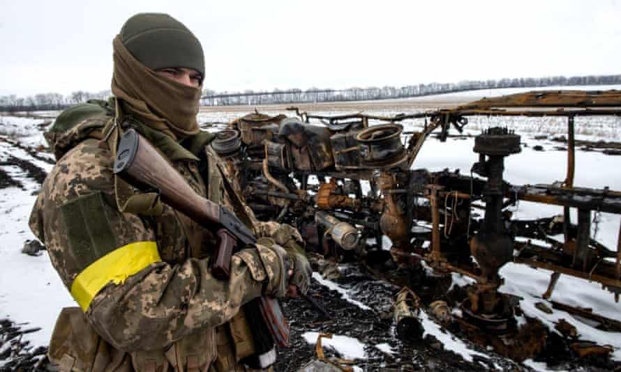 soldier with gun and yellow armband stands next to supplies