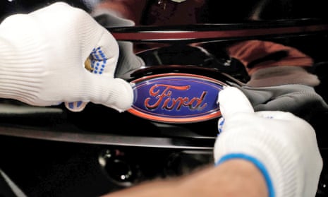 Gloved hands attaching a Ford logo to a car