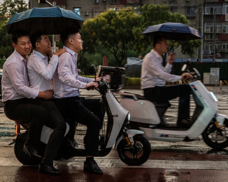 Beijing office workers, three on one scooter, one on another, umbrellas up