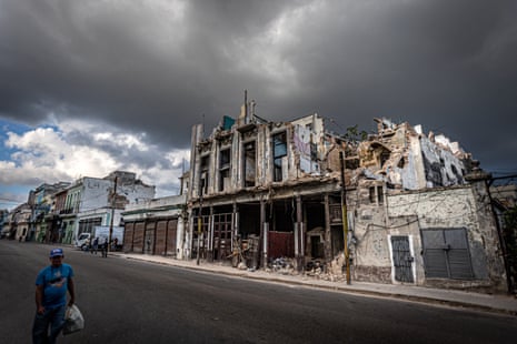 A man walks through the centre of Havana in front of a collapsed block of buildings, a common sight