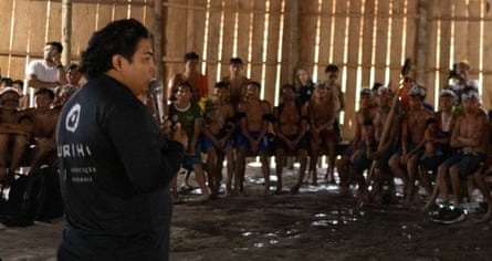 Júnior Hekurari speaking to Yanomami villagers in a large room