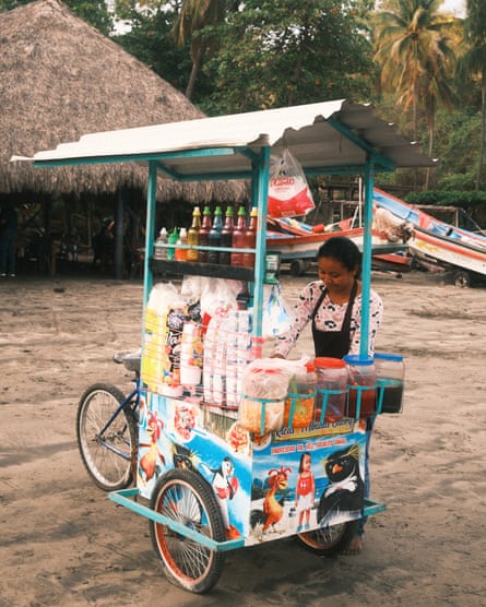 A woman stands at a small stall on wheels preparing to serve snacks