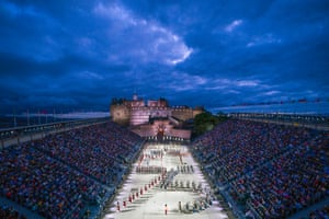An aerial dusk shot of soldiers in ceremonial uniform marching in formation in an arena with Edinburgh Castle in the background