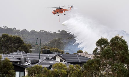A skycrane drops water on a bushfire in scrub behind houses in the Melbourne suburb of Bundoora.