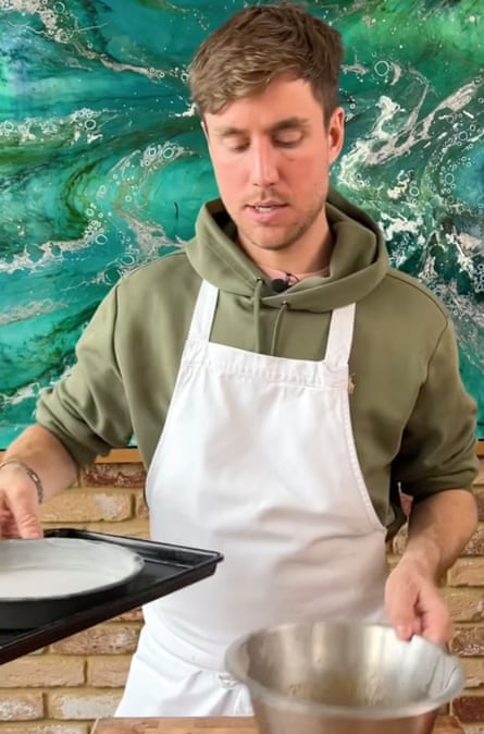 Matthew Ryle in a hoodie and apron holding a pan on a tray in one hand and a metal bowl in the other