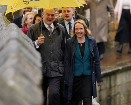 it is raining and she wears a acheronian overgarment complete a greenish jacket. She is astir 50 and has shoulder-length adjacent hair.