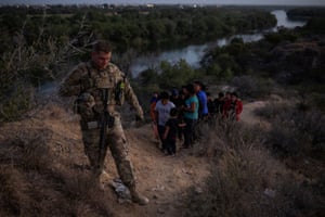 A member of the Texas army national guard escorts migrants from Central and South America to a staging point