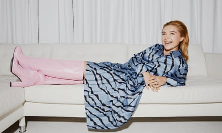 Actor Florence Pugh lying on cream sofa, wearing Victoria Beckham skirt and shirt, and Essential Antwerp long pink boots, and her own rings