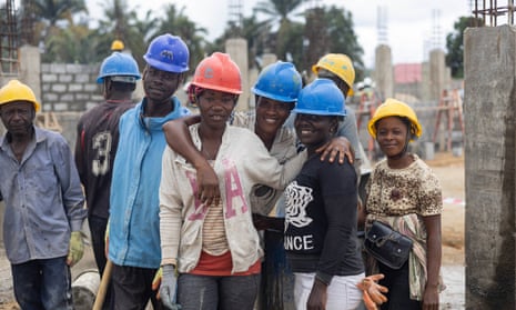A group of mainly female construction workers pose for the camera in hard hats on a building site in Sierra Leone