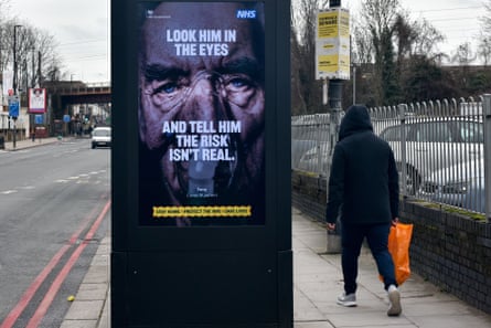 A government/NHS billboard on a London street shows a man on a ventilator and carries the message: 'Look him in the eyes and tell him the risk isn’t real'