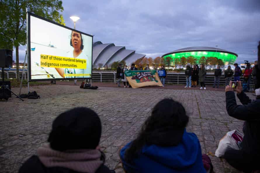 People gathered outside around a large screen portraying a murdered environmental defender