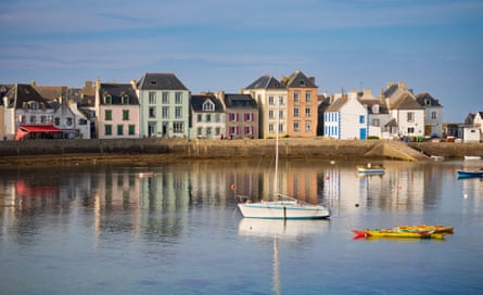 A row of colourful houses on the seashore, refected in blue water, with a small boat in the foreground