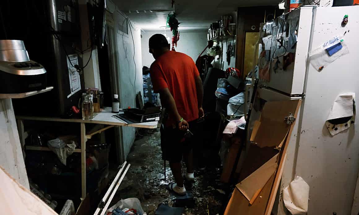 Eddie, dressed in a red shirt, walks through a flooded and wrecked basement-level apartment with his back to the camera