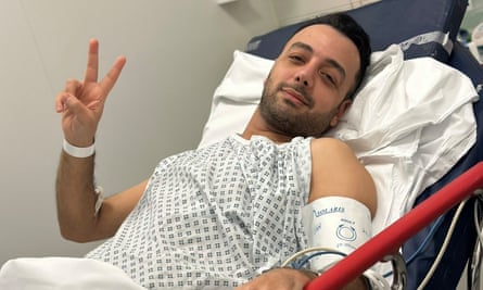 A man in a hospital bed holds up his hand in a V sign.