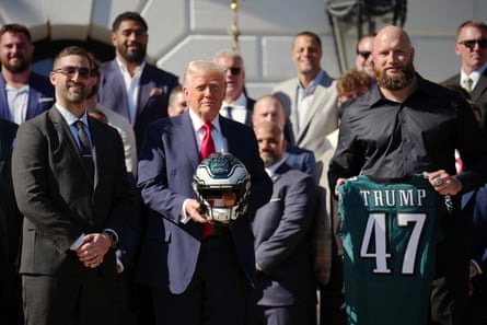 Donald Trump holds a football helmet while posing with the Philadelphia Eagles, while one member holds a #47 jersey that says Trump