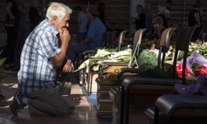 A man kneels before the coffin of a relative before the state funeral in Ascoli Piceno of earthquake victims
