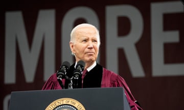 White man wearing red and black robes stands in front of podium and microphone