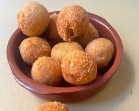 A brown bowl of cheese and bread balls with a couple scattered on the surface.