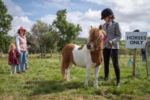 A girl in riding gear stands in a field with her pony as a family behind her look on