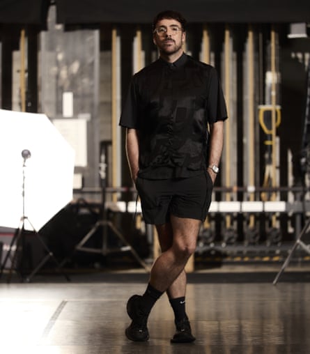 Marcos Morau stands in a black shirt and shorts on a studio floor near photography lighting equipment
