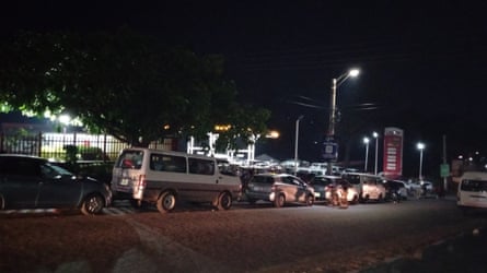 Under streetlights, a long line of minibuses, cars and taxis queues along the dark highway for fuel in Zomba, Malawi.