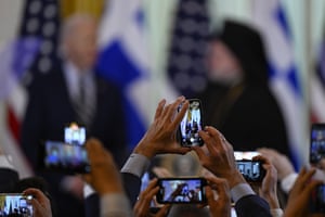 People hold up smartphones to take pictures of Joe Biden and Archbishop Elpidophoros
