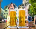 Two tall glasses of beer sit on an outdoor table in Cologne, with colourful buildings behind