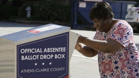 A voter drops their ballot into an official Absentee Ballot drop box