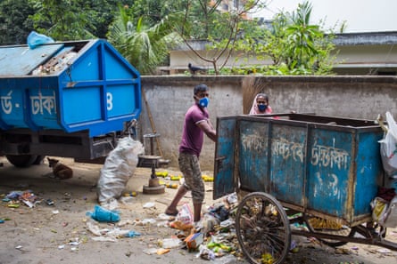 A masked refuse collector empties a rubbish cart