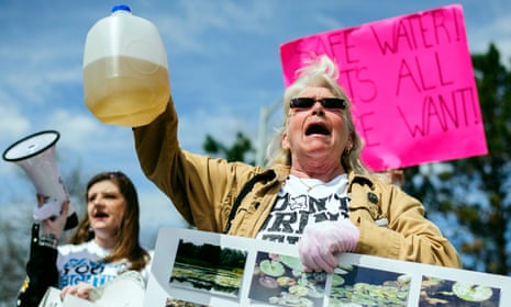 Protesters hold up jugs of discolored water outside the Farmers Market in Flint, marking the one year anniversary of the city switching from using Detroit water to Flint River water.