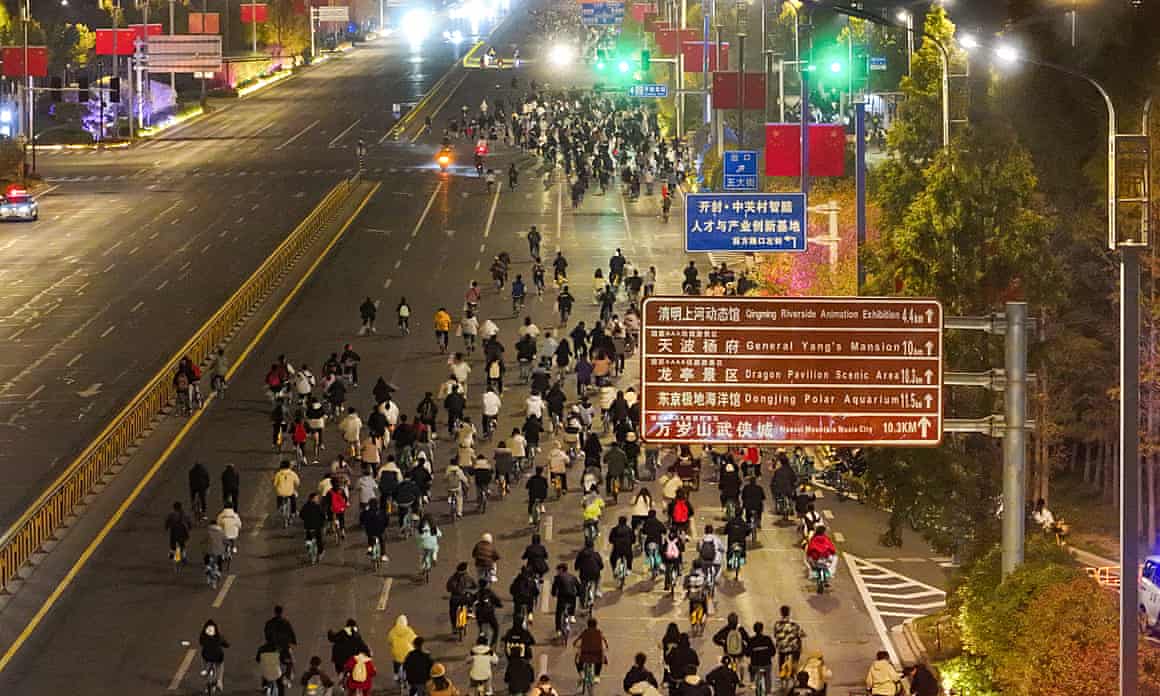View looking down on cyclists making their way along a wide, multi-lane road at night