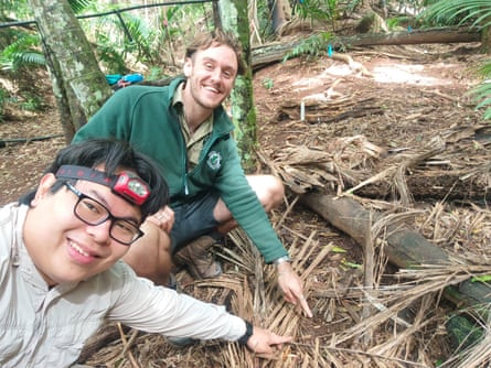 Junn Kitt Foon and Sam Burridge point to a tiny snail on the ground in the native forest