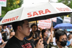 A man holds an umbrella printed with the slogan ‘Convict Sara Now!’