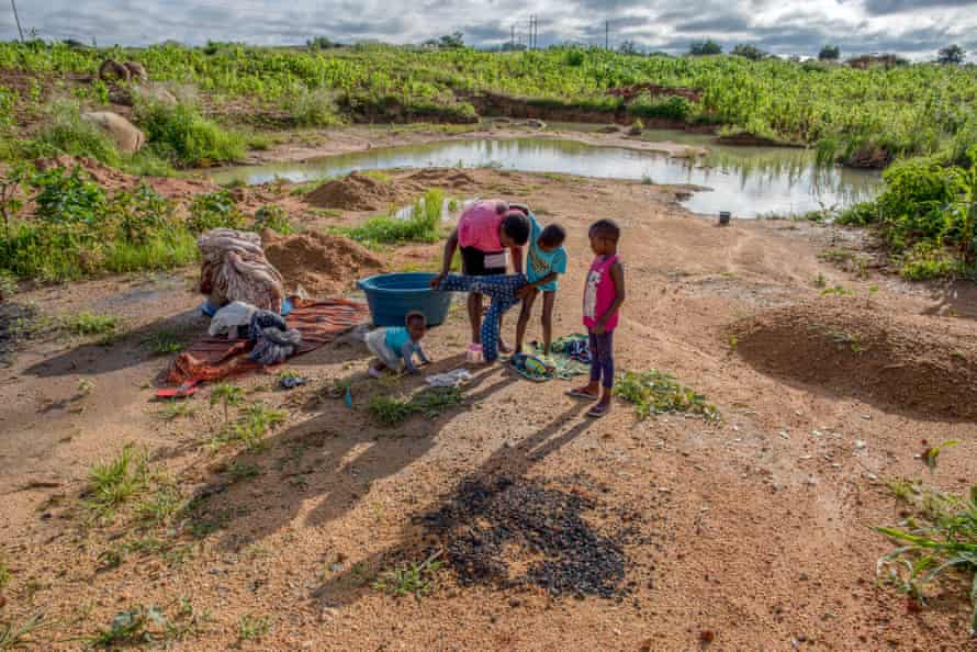 A woman helps her children get dressed after taking a bath in a pond in Hopley