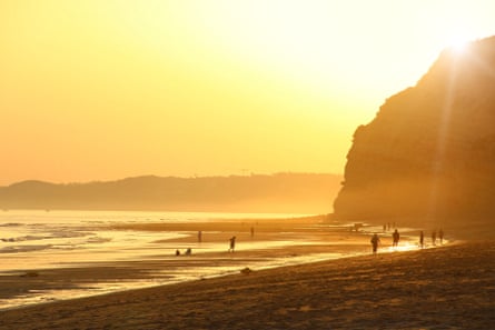 A beach bathed in a yellow sunset with cliffs to one side