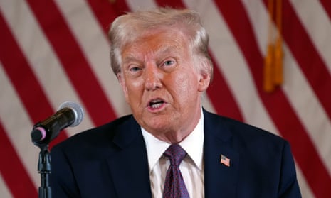 close-up of man wearing navy suit and patterned tie speaking behind microphone