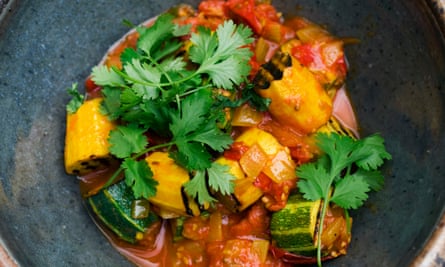 A rustic bowl with chopped courgettes and tomatoes, topped with sprigs of coriander.