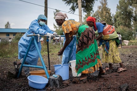 Women wash their hands under temporary outdoor taps as staff in protective gear look on