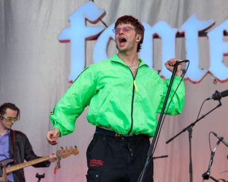 Grian Chatten sings into a microphone on stage, wearing a neon green jacket
