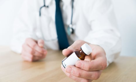 Doctor sitting at desk wearing stethascope handing patient a bottle of medicine