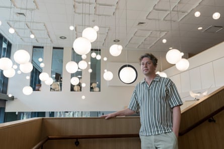 Artistic director Tony Guillan stands in the gallery with hanging lights behind him