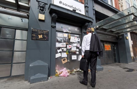 A man reads placards left on the doors of the Fabric night club. There are bunches of flowers at the base of the doors.