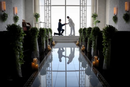 A gay couple in black and white suits pose for wedding photos in a chapel