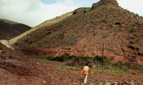 A person in a hi-vis jacket walking away from the camera towards a large dirt mound or hill