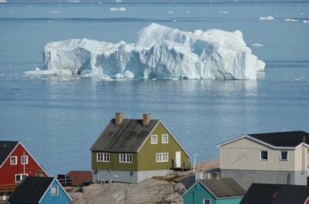 An iceberg floats in Disko Bay behind houses in Ilulissat, Greenland.