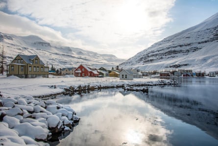 lakeside houses in different colours with sloping roofs are clustered around an icy lake at the foot of mountains