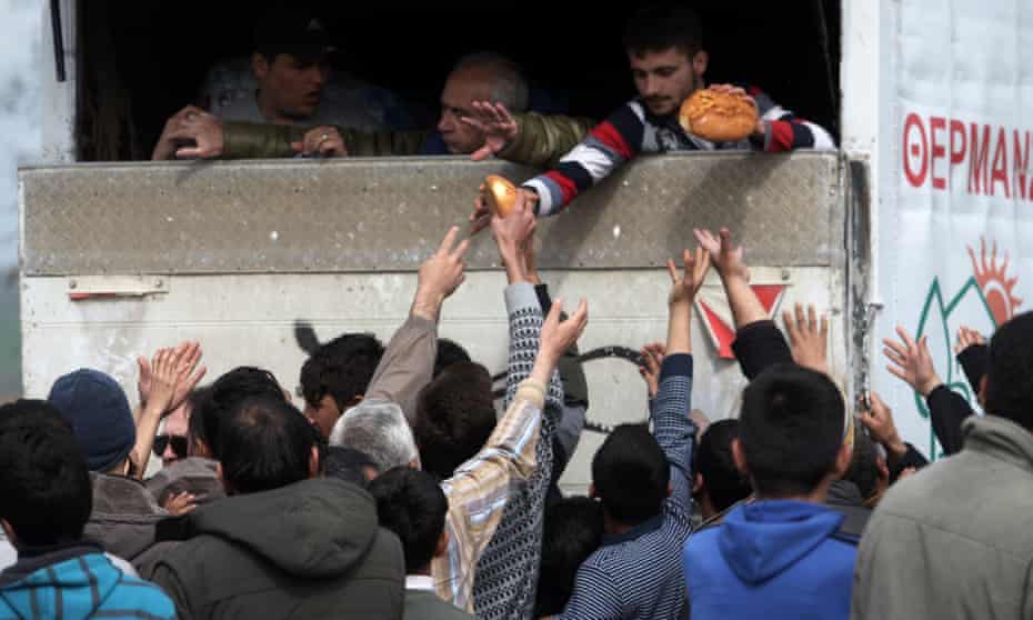 Volunteers give bread to migrants at a makeshift camp near the Greek village of Polykastro
