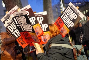 a person standing outside holds several signs that say ‘Dump Trump, fight bigotry'