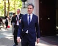 Foreign Secretary Ed Miliband smiles while walking outside, with two men behind him
